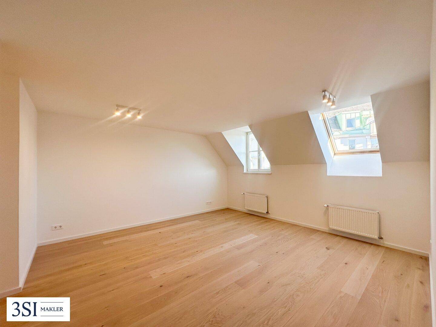 Geräumiger, leerer Raum mit Holzboden, Dachschrägen und viel Tageslicht durch die Fenster, vielseitig nutzbar.