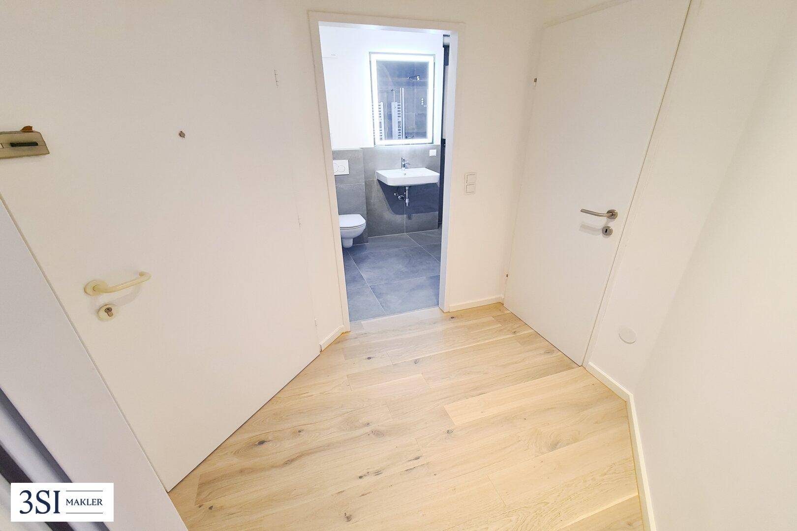 Heller Flur mit Parkettboden, der zu einem modernen Badezimmer führt.