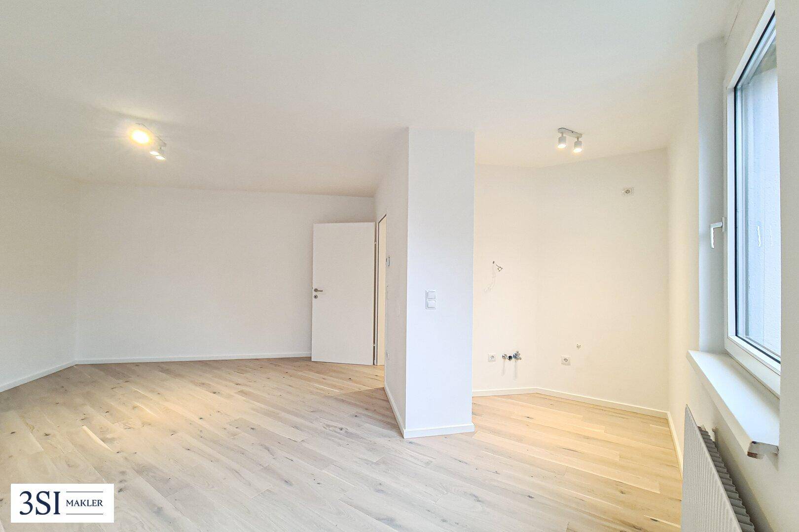 Heller Wohnbereich mit Holzboden und Anschlüssen für eine mögliche Küchenzeile in der Ecke.