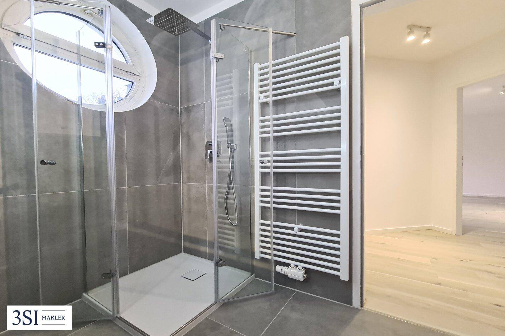 Duschbereich im modernen Badezimmer mit Regendusche, Handtuchheizkörper und ovalem Fenster.