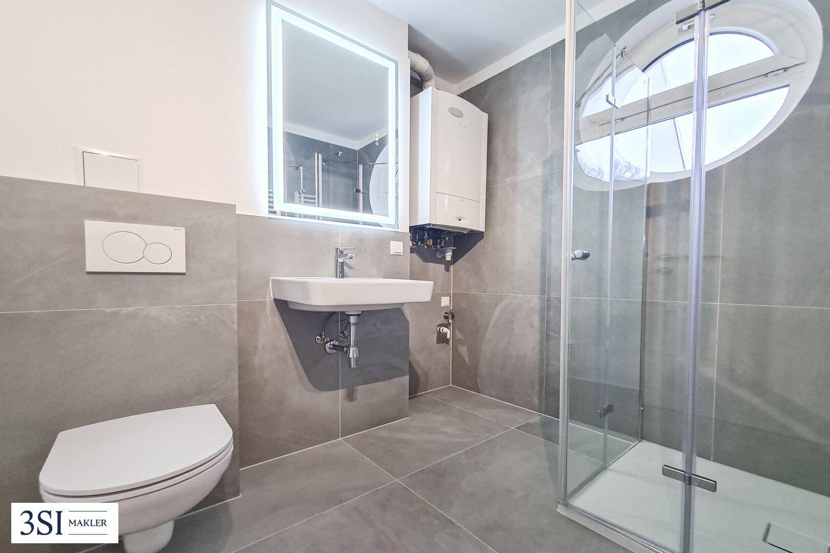 Modernes Badezimmer mit grauen Fliesen, wandhängendem WC und einer Duschkabine mit ovalem Fenster.
