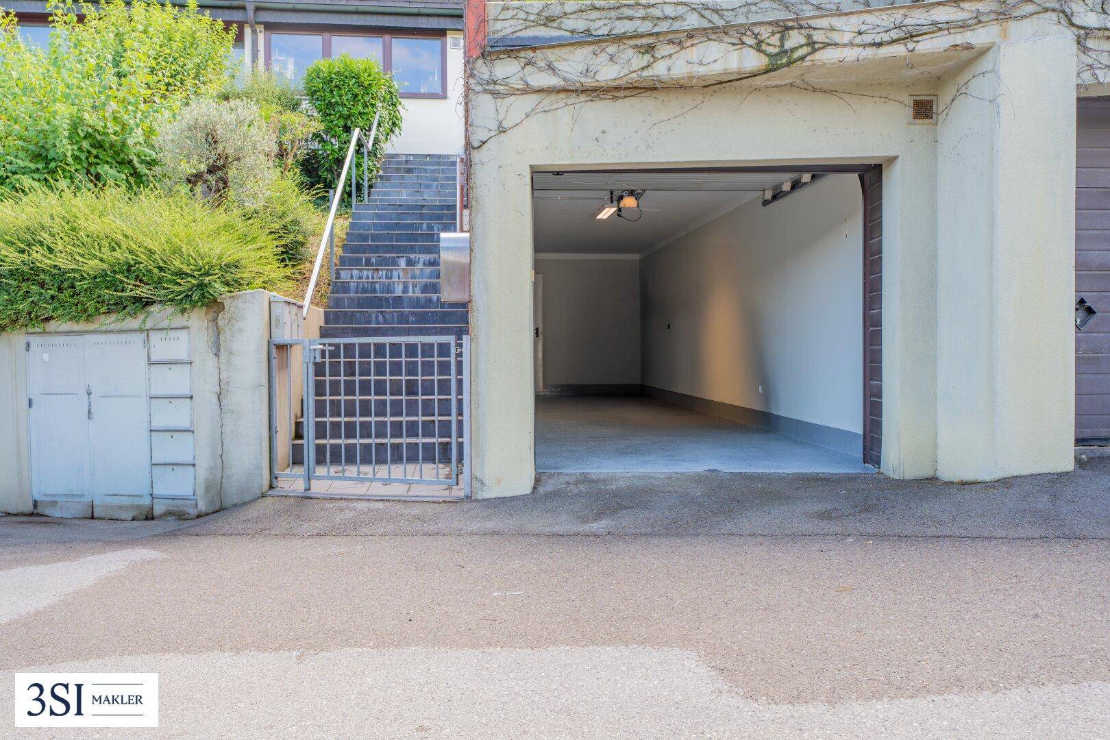 Leere Garage mit offenem Tor und einer Treppe, die zum Haupteingang des Hauses führt.