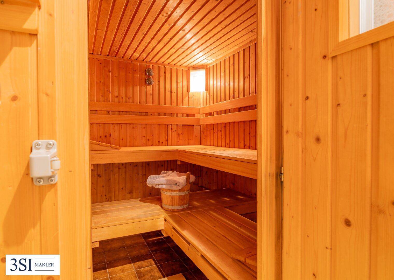 Traditionelle Holzsauna mit mehreren Sitzbänken und einem Eimer für Aufgüsse.