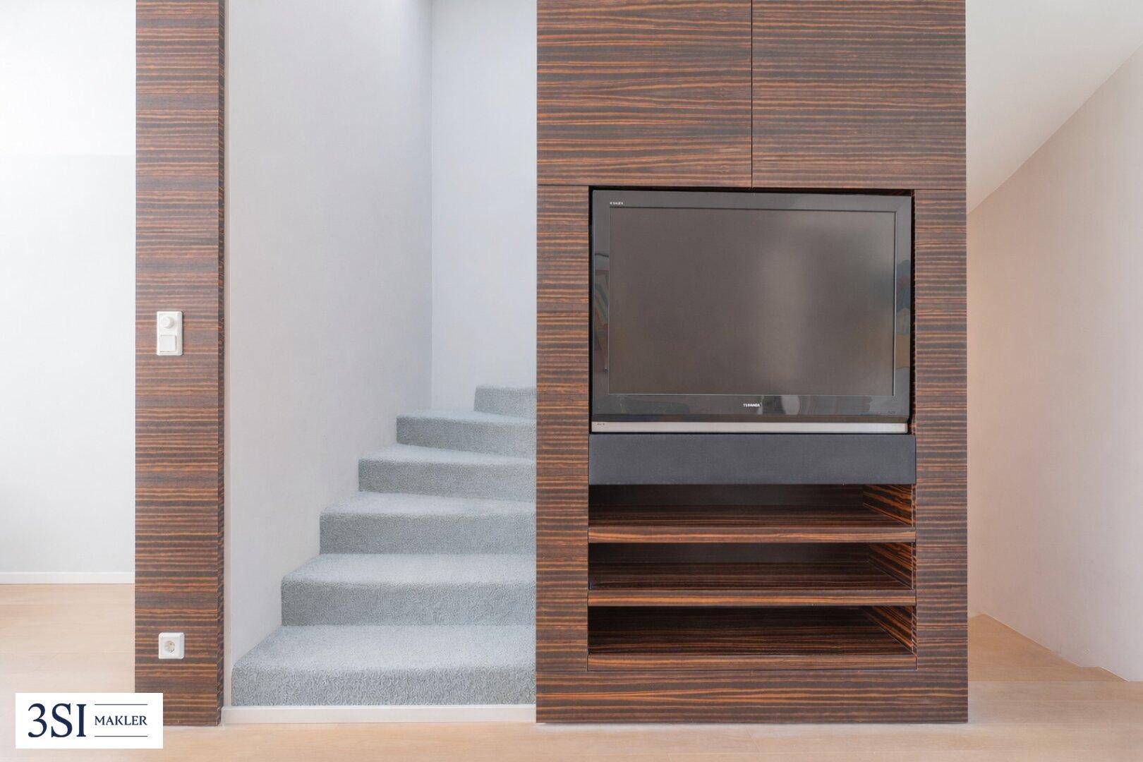 Eingebauter Fernsehbereich mit Holzvertäfelung und Regalen neben einer mit Teppich belegten Treppe.