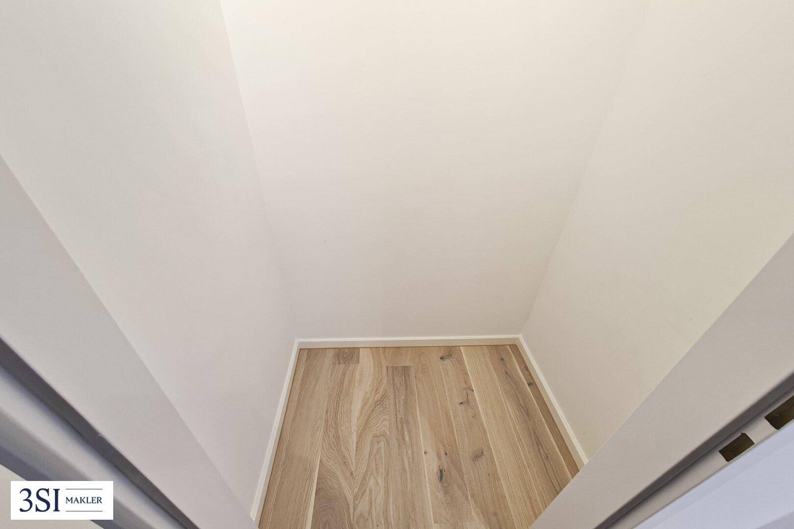 Kleiner, leerer Abstellraum mit hellem Holzfußboden und weißen Wänden, ideal für zusätzlichen Stauraum.