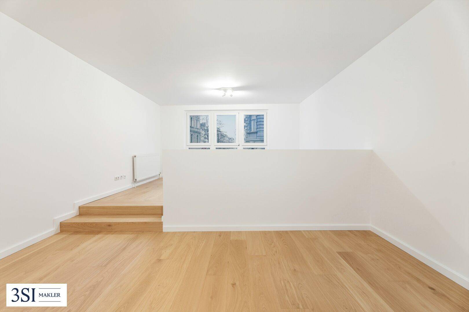 Heller Raum mit Parkettboden und einer kleinen Treppe zu einem erhöhten Bereich.