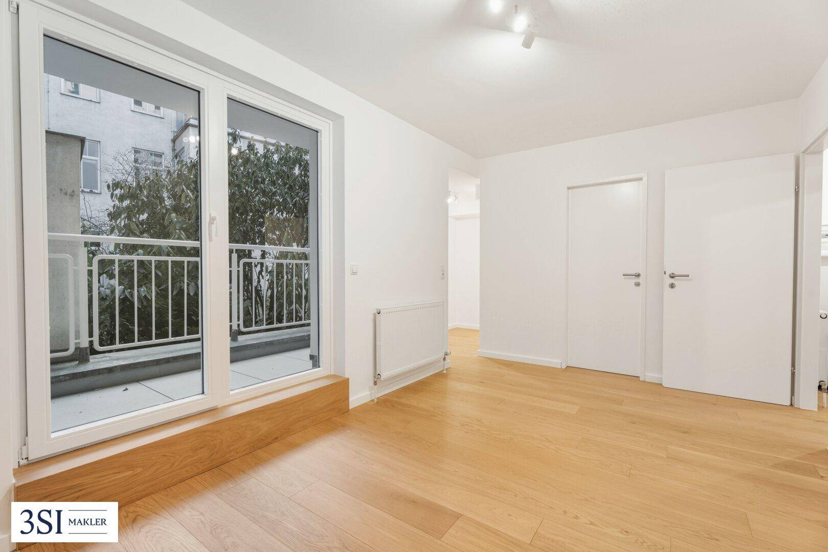 Heller Raum mit Parkettboden und Zugang zu einem kleinen Balkon mit Grünblick.