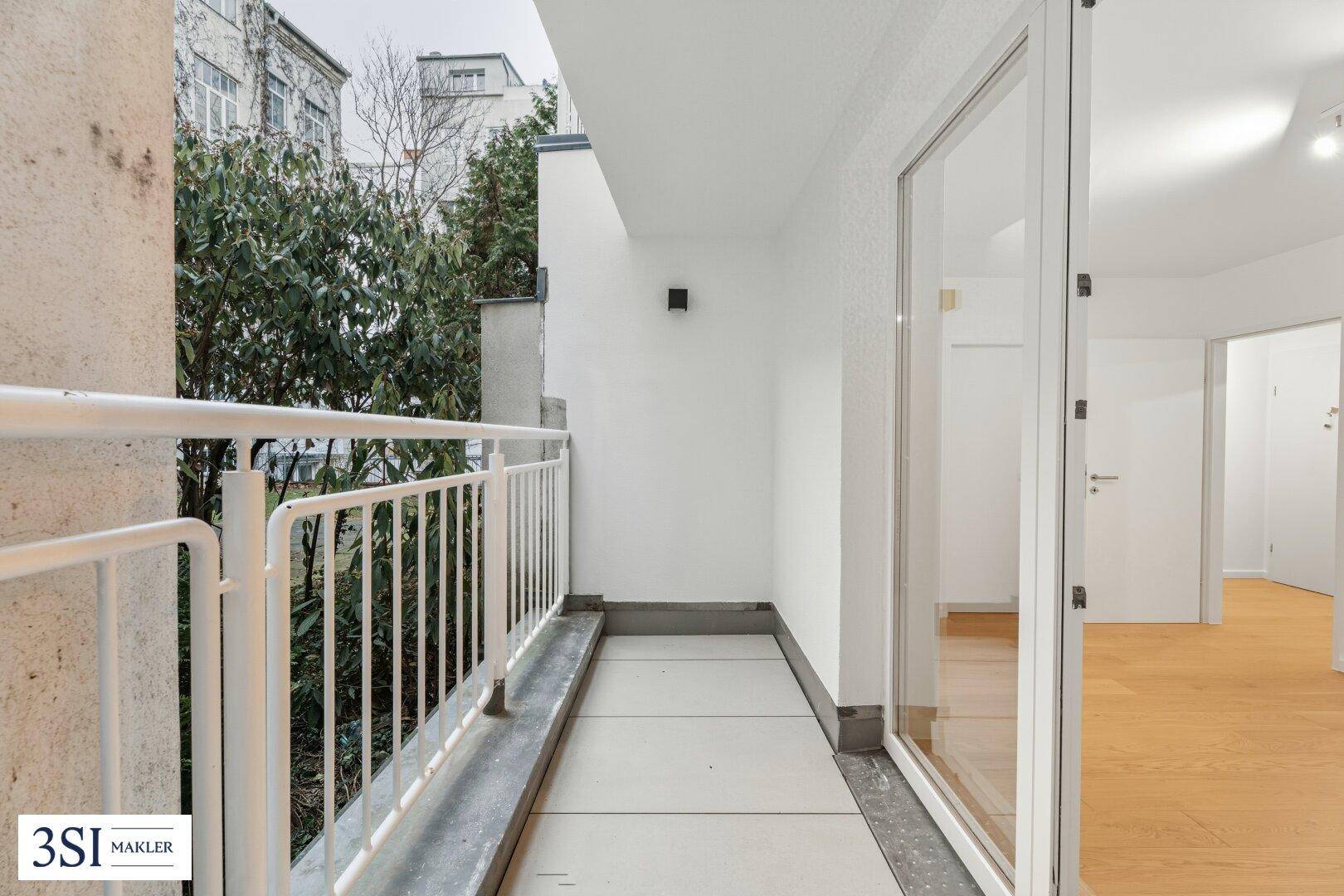 Schmaler Balkon mit Metallgeländer und Blick auf Bäume und umliegende Gebäude.