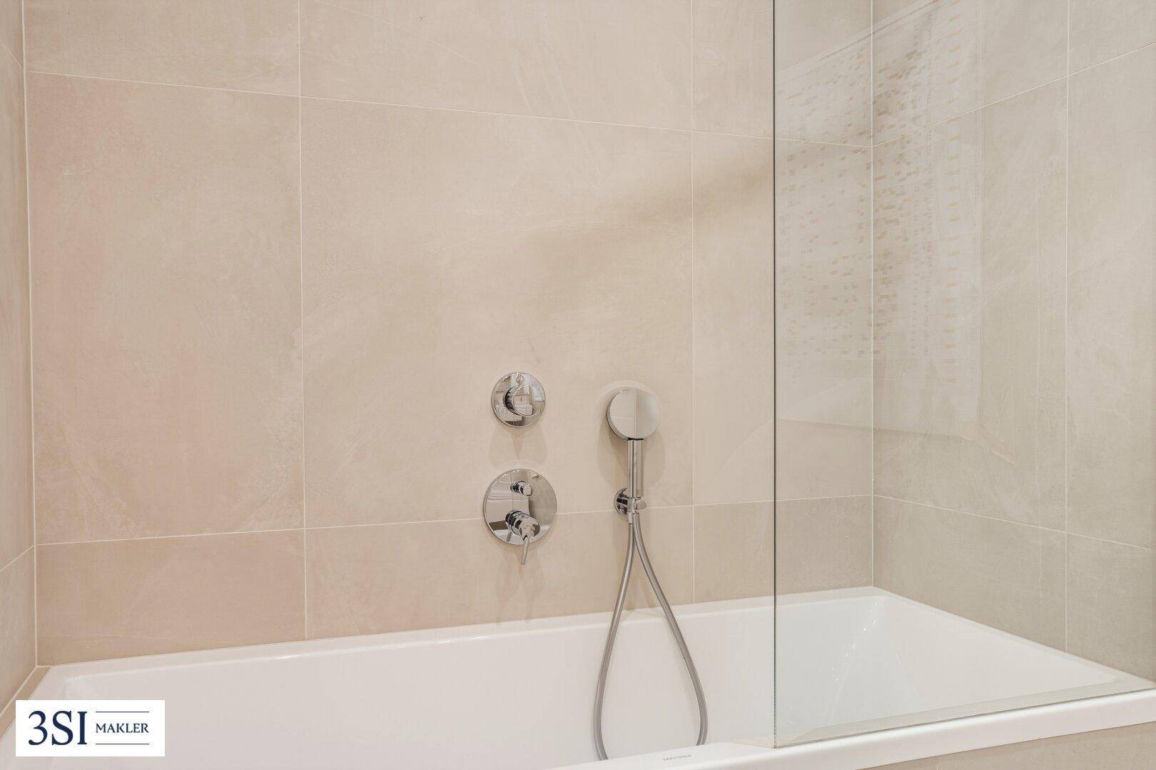 Modernes Badezimmer mit Badewanne, Duscharmatur und hellen Fliesen.