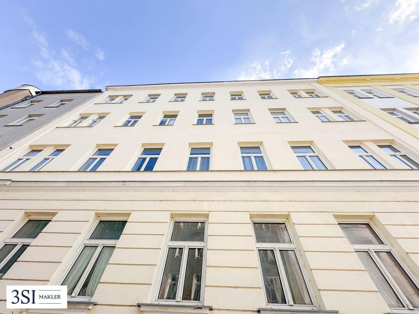 Klassische Fassade eines Altbaus mit vielen Fenstern unter blauem Himmel.