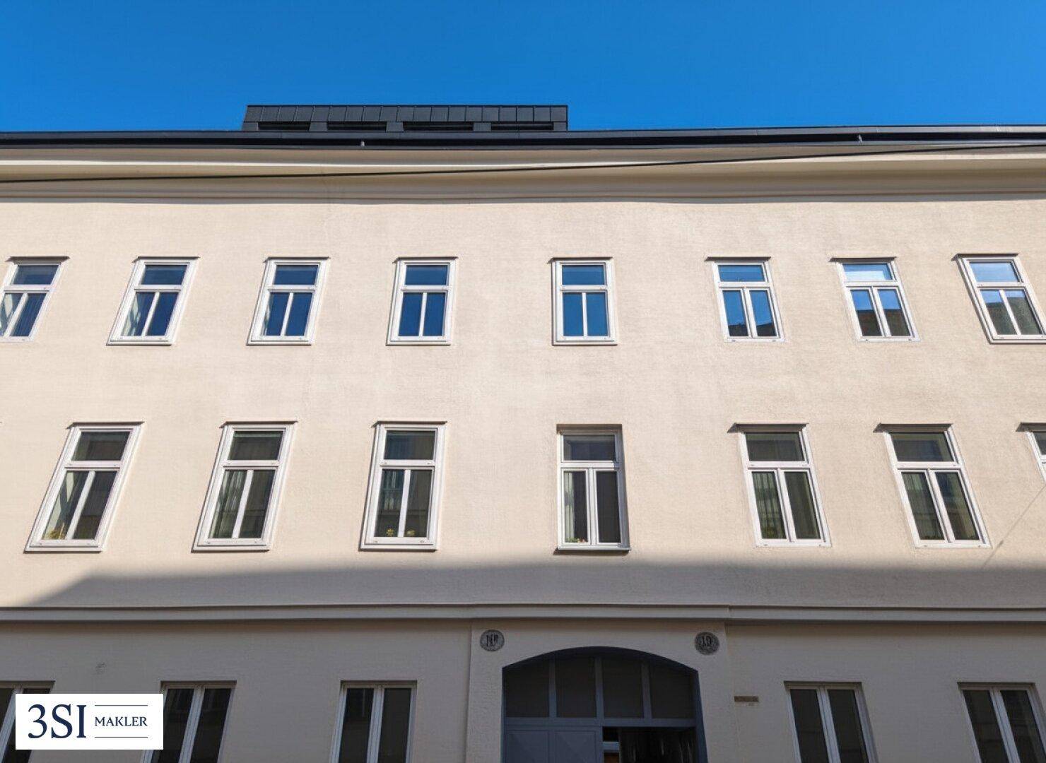 Klassische Fassade eines Mehrfamilienhauses mit vielen Fenstern unter blauem Himmel.