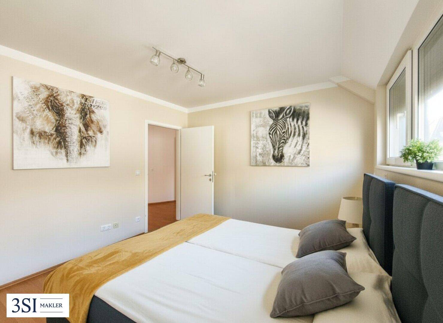 Helles Schlafzimmer mit Doppelbett, Laminatboden und einem Fenster für natürliche Belichtung.