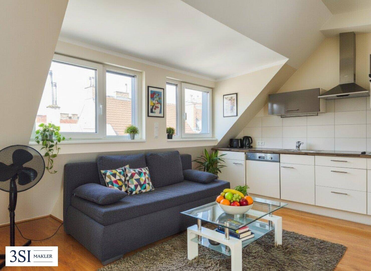 Gemütliches Wohnzimmer mit integrierter Küchenzeile, Sofa und großen Fenstern für viel Tageslicht.