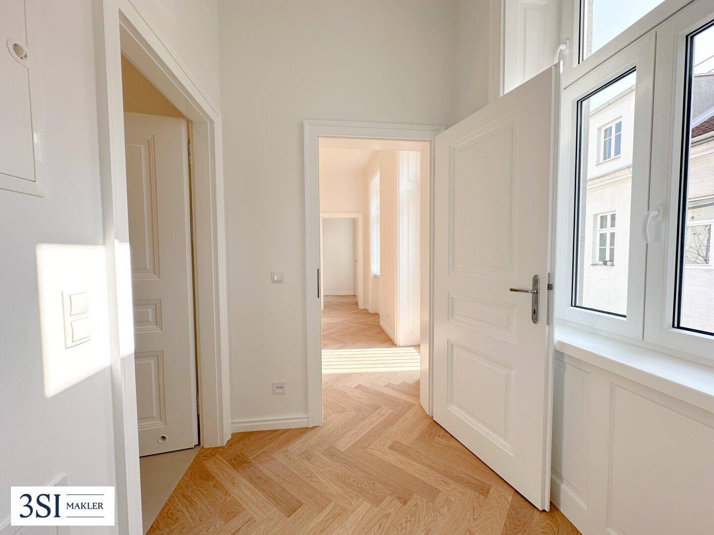 Heller Flur mit Fischgrätparkettboden und offenen Türen, die den Blick in weitere Zimmer freigeben.