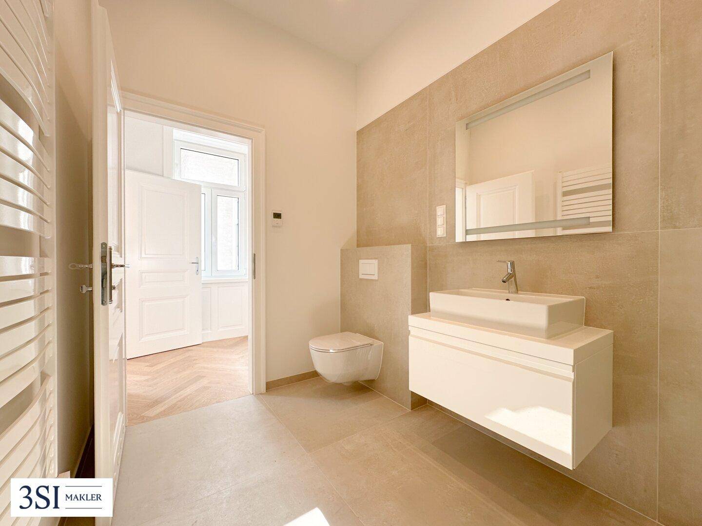 Modernes Badezimmer mit beigefarbenen Fliesen, wandhängendem WC, Einzelwaschbecken und beheiztem Handtuchhalter.