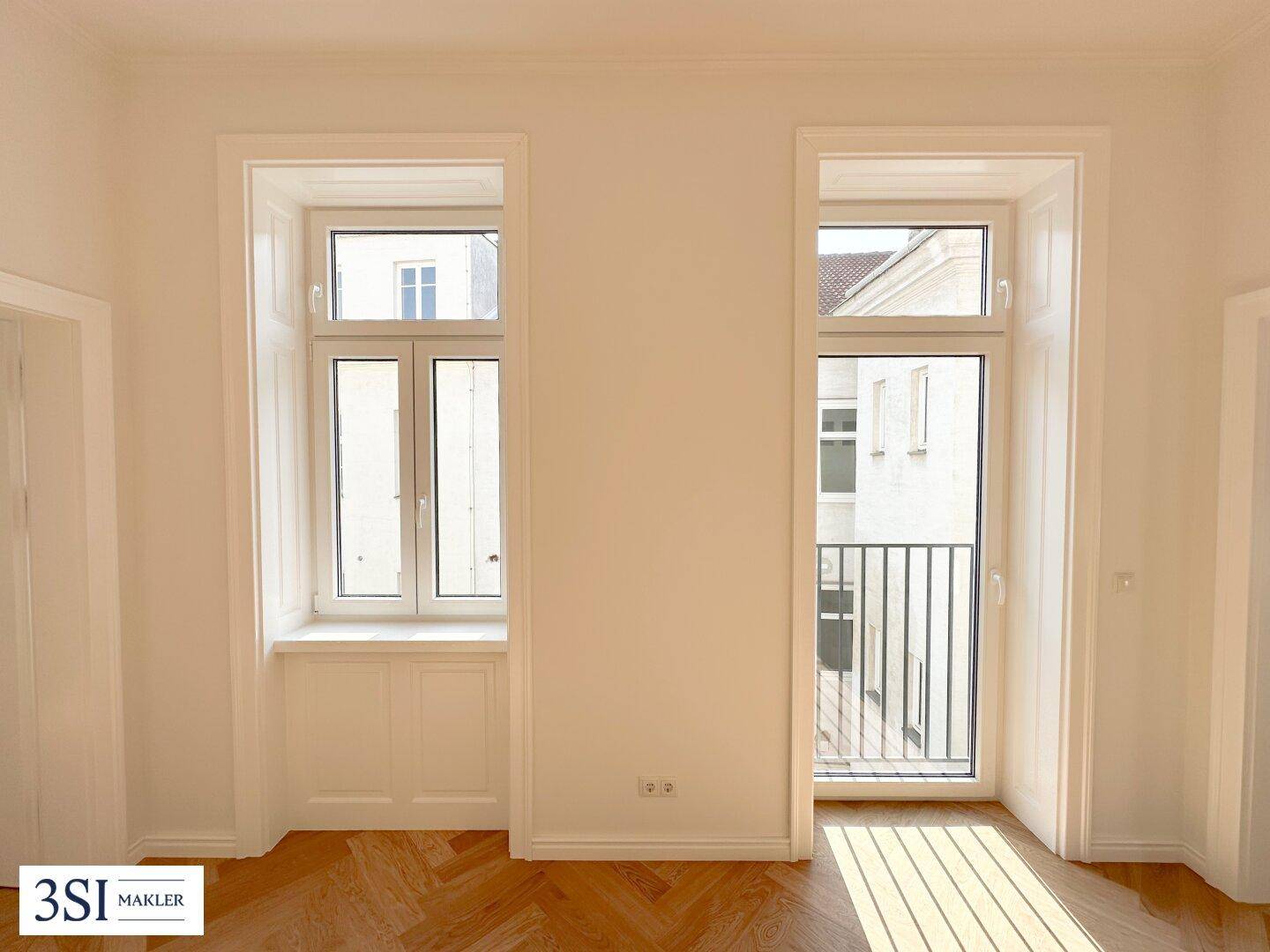 Detailansicht der großen Fenster, eines davon mit einem eleganten französischen Balkon und viel Tageslicht.