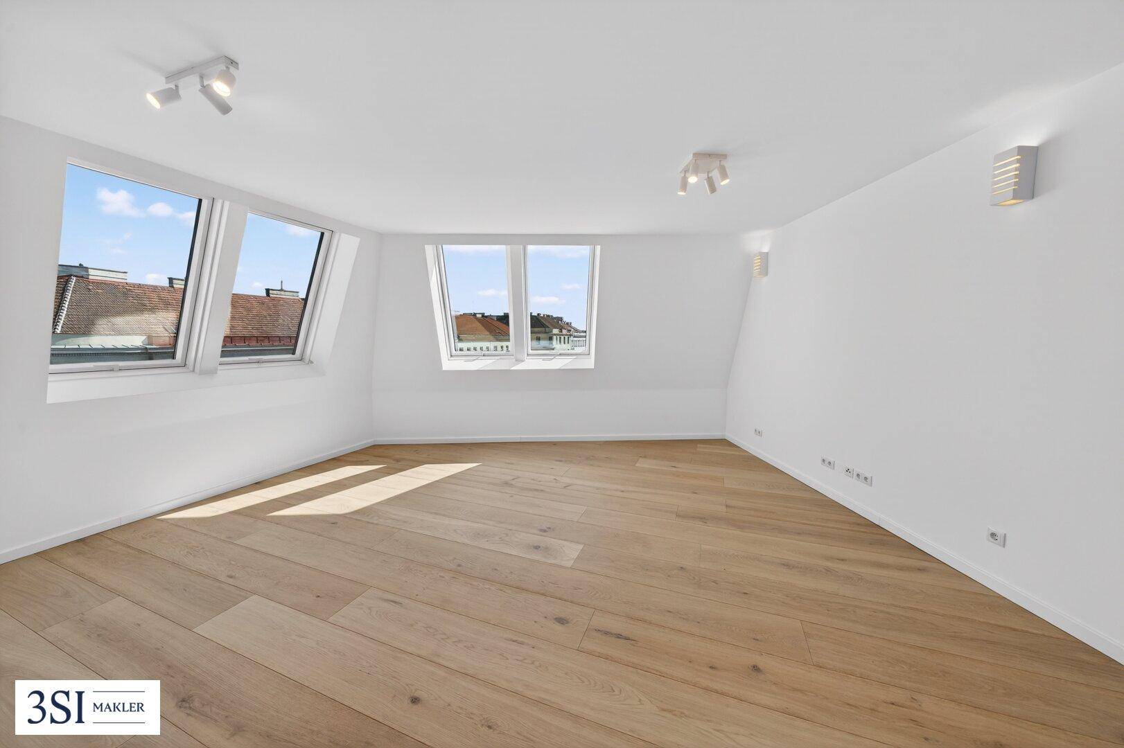 Heller Dachgeschossraum mit Holzboden, schrägen Wänden und großen Dachfenstern.