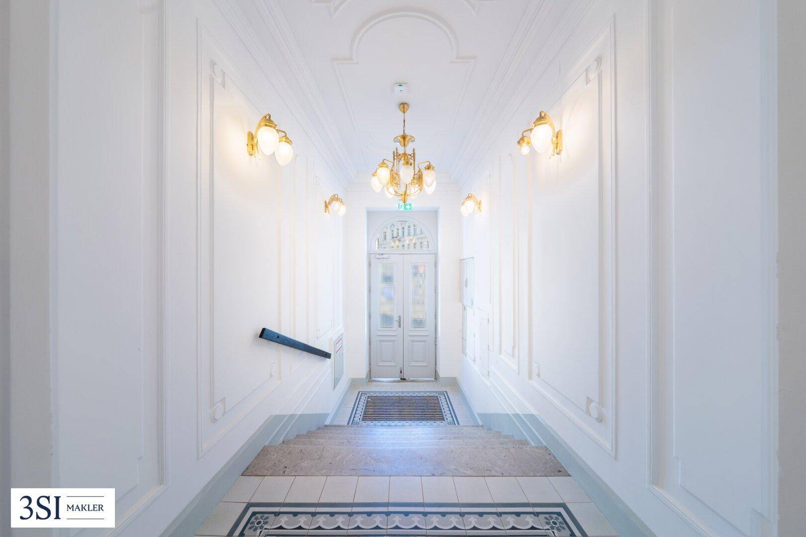 Eleganter Eingangsbereich mit Stuckdecke, Wandleuchten und einer Treppe mit Fliesenboden.