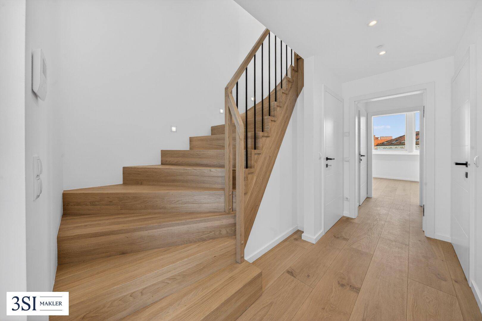 Moderne Holztreppe in einem hellen Flur mit Parkettboden und weißen Wänden.