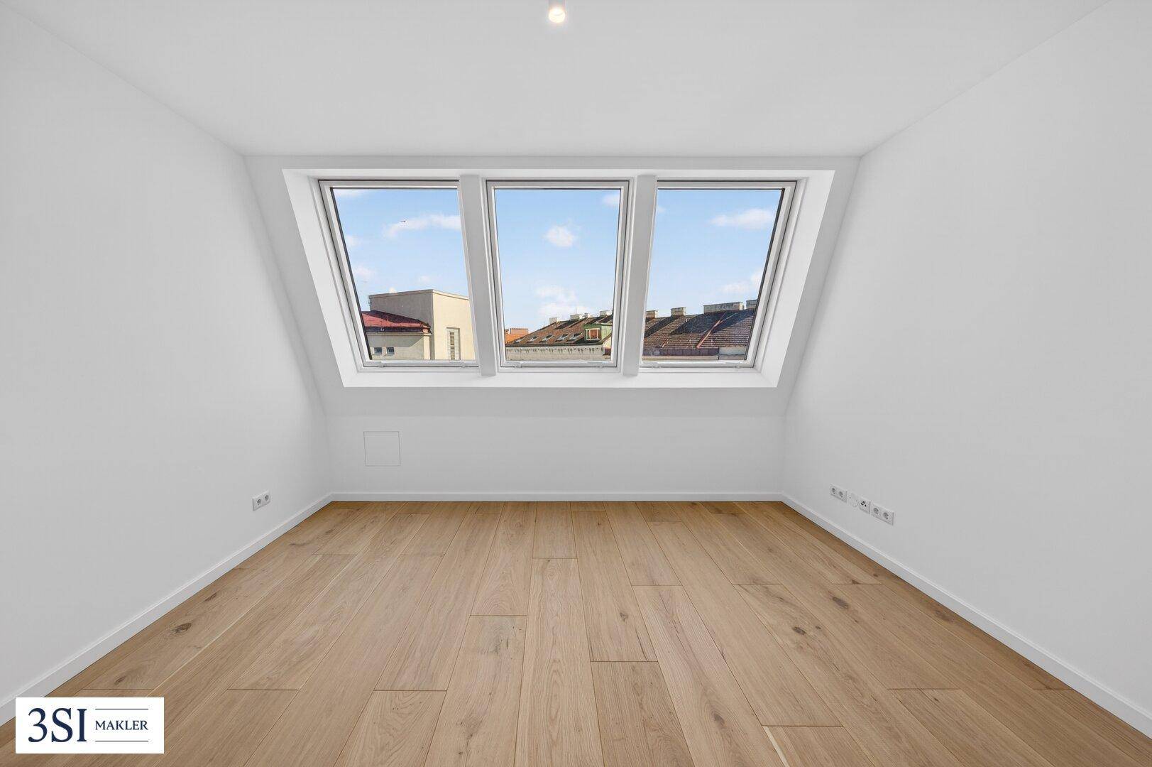 Helles Zimmer mit Dachschrägen, Holzboden und großen Fenstern mit Blick auf die Stadt.