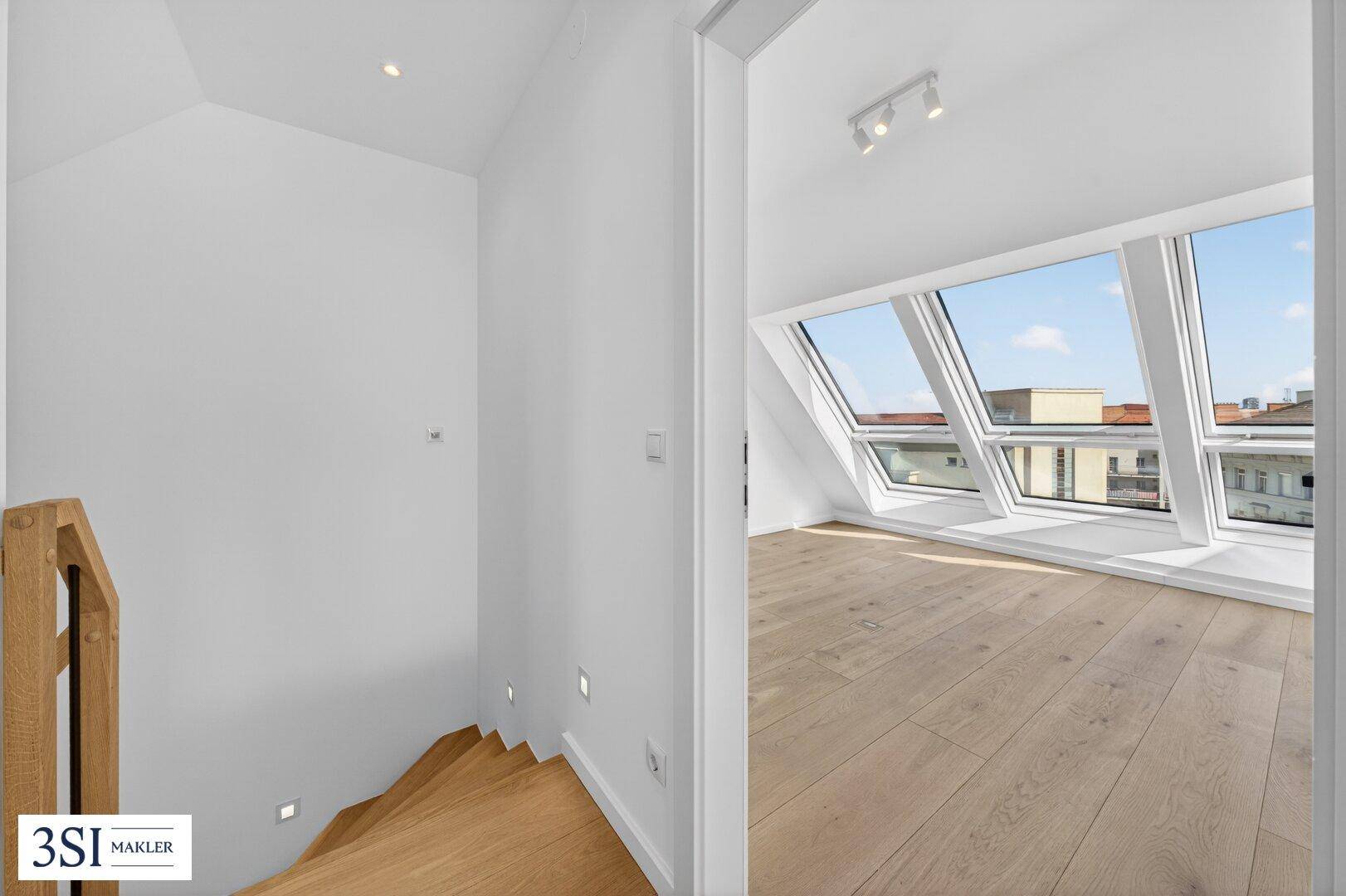 Moderne Holztreppe führt zu einem hellen Raum mit Dachfenstern und weiß gestrichenen Wänden.