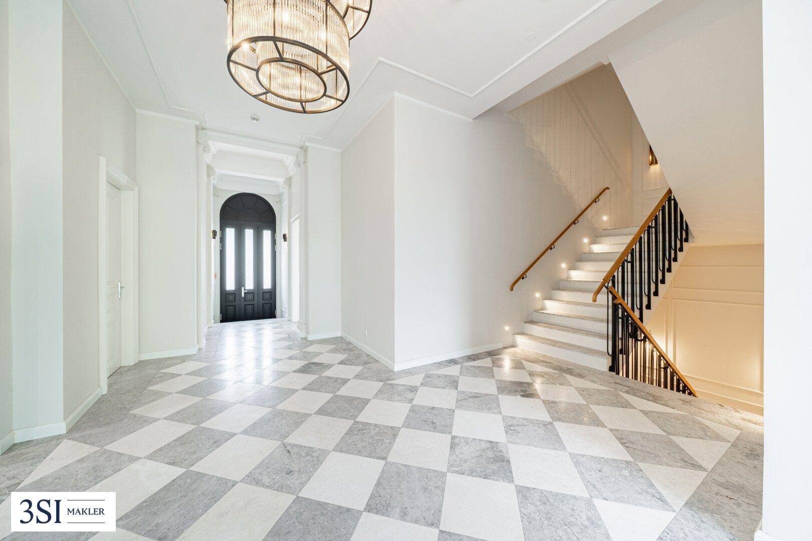 Eleganter Flur mit Marmorboden, geschwungener Treppe und Blick auf die Eingangstür.