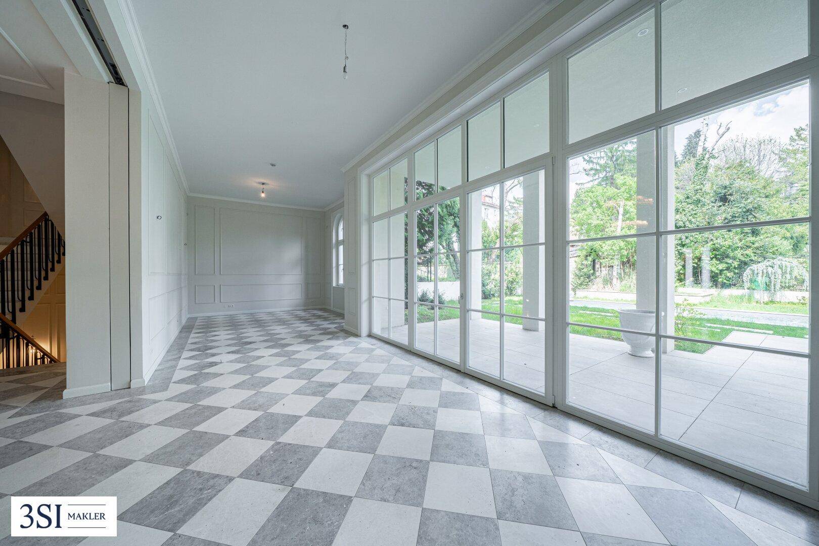 Heller Eingangsbereich mit Schachbrettmuster-Marmorboden und großen Fenstern zum Garten.