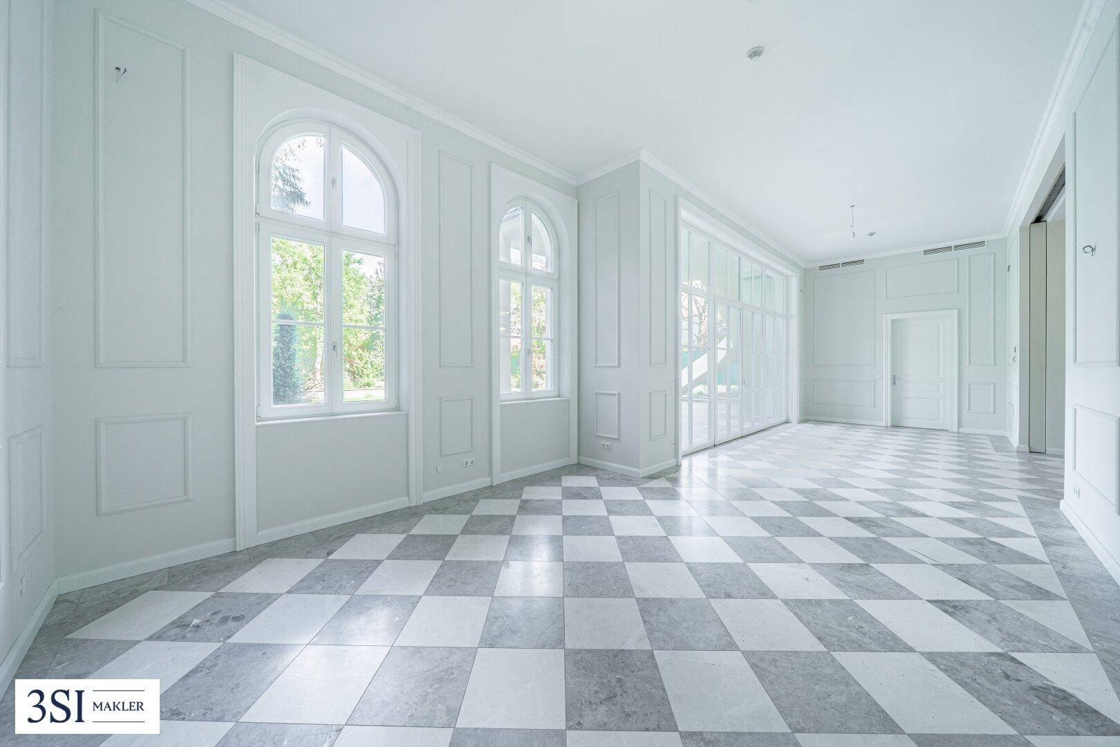 Heller Raum mit Marmorboden und eleganten Rundbogenfenstern mit Blick ins Grüne.
