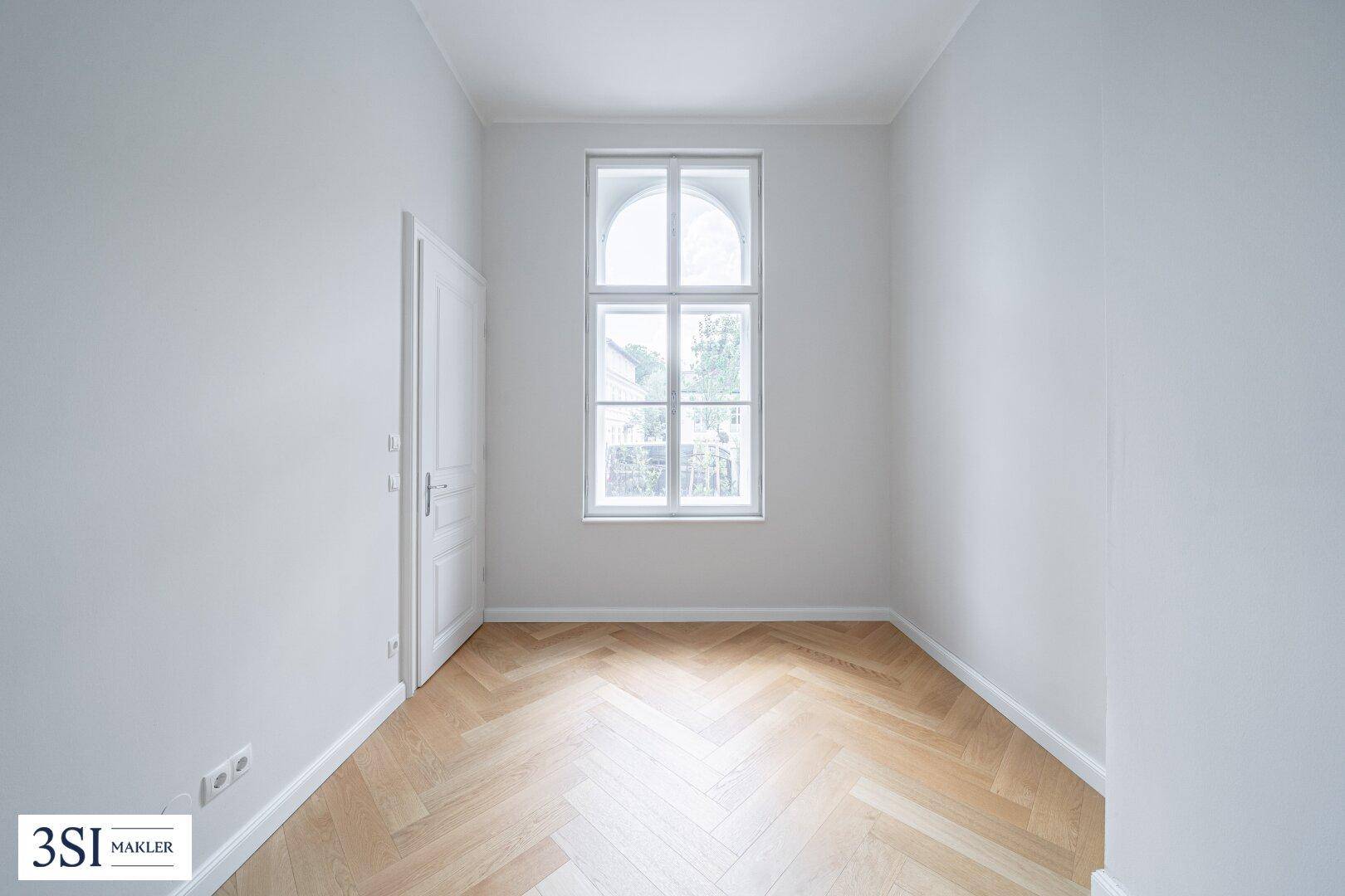 Kleiner, heller Raum mit Fischgrätparkett und einem eleganten Rundbogenfenster.