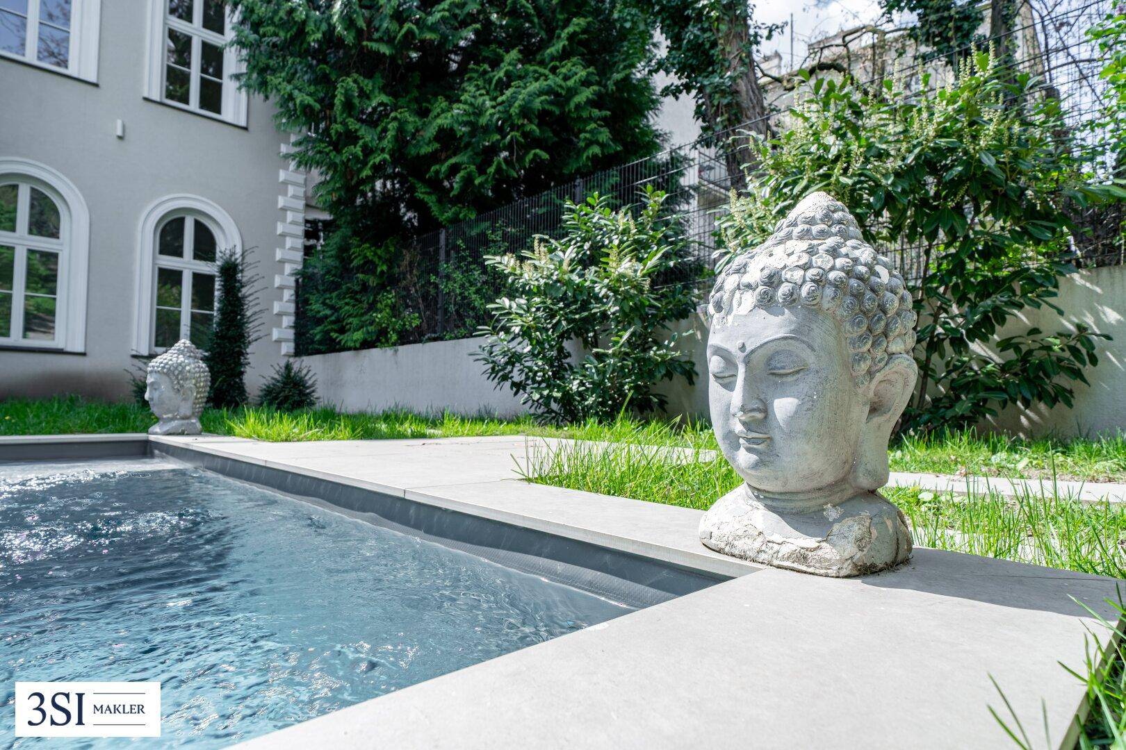 Dekorative Buddha-Statue am Rande des Swimmingpools im gepflegten Gartenbereich.