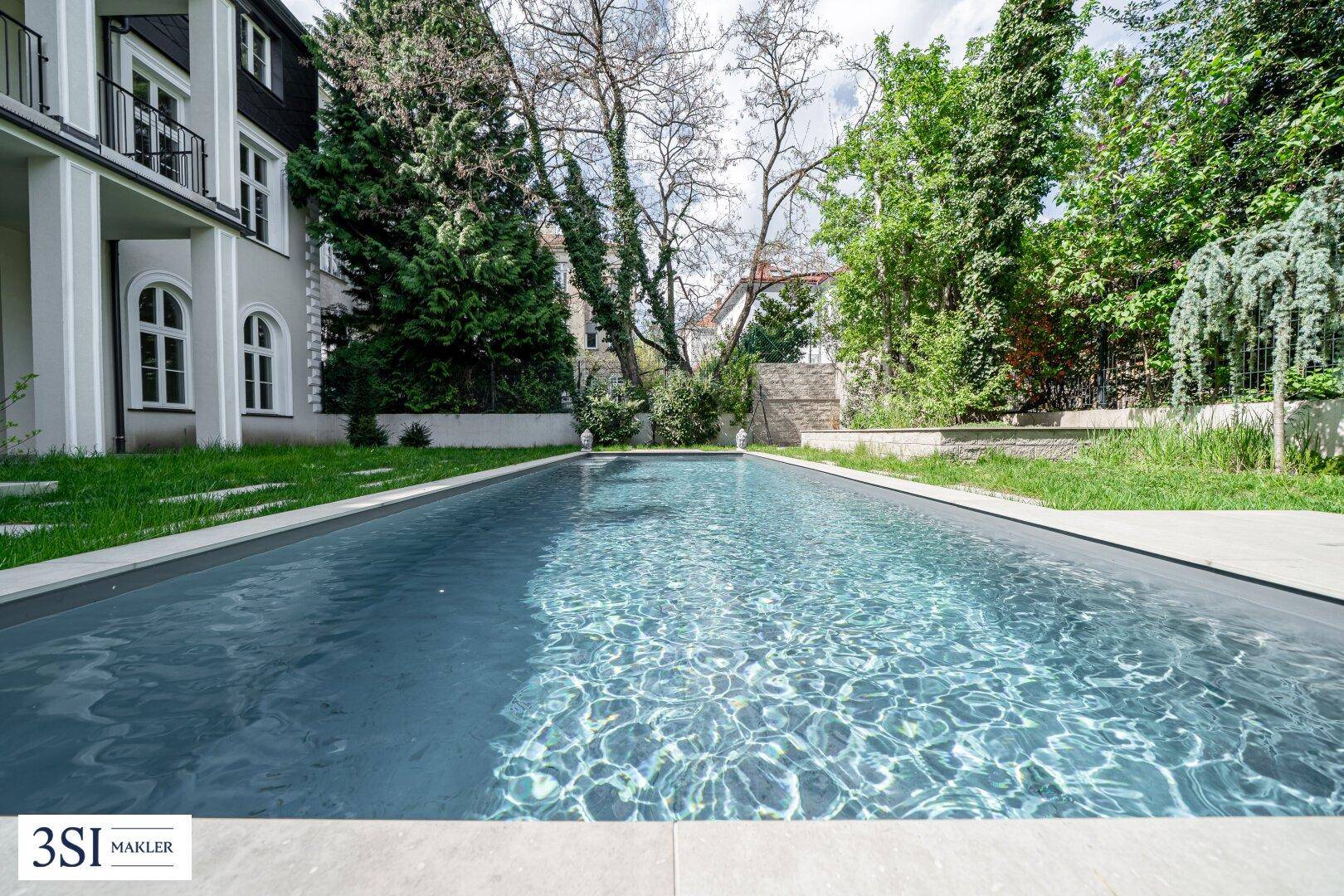 Langer Swimmingpool im Gartenbereich, umgeben von gepflegtem Grün und Bäumen.