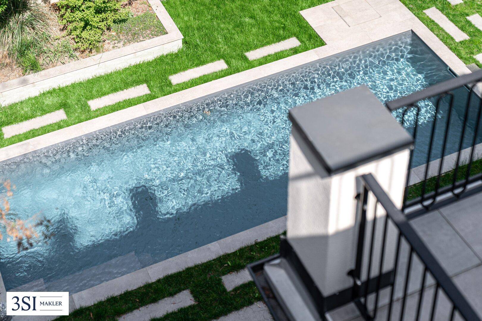 Blick von oben auf den eleganten Swimmingpool im Garten mit umliegenden Grünflächen.