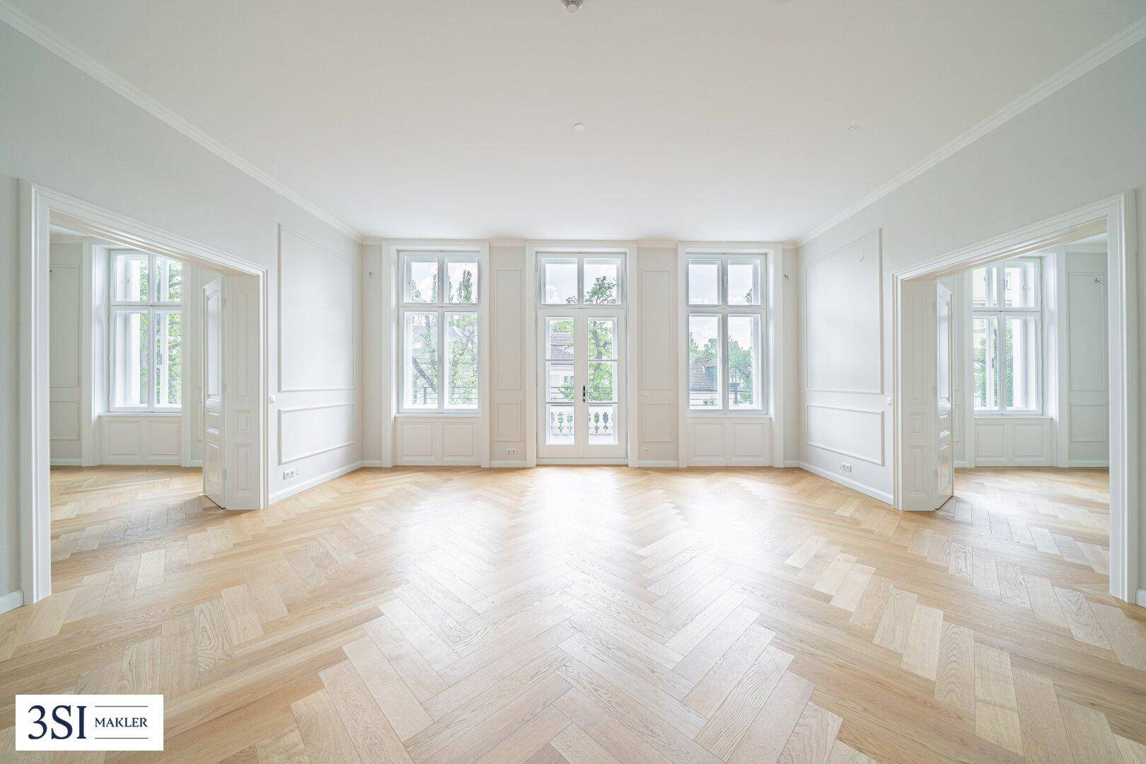 Großzügiger Wohnbereich mit Fischgrätparkett, hohen Fenstern und einem französischen Balkon.