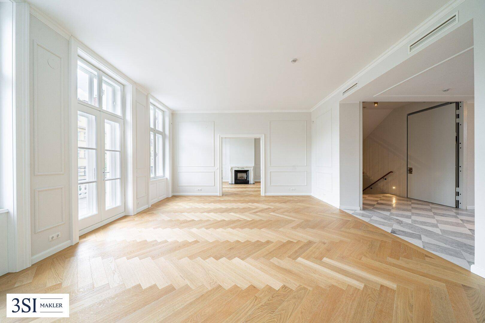 Geräumiges Wohnzimmer mit elegantem Fischgrätparkett, hohen Fenstern und dekorativen Wandpaneelen.