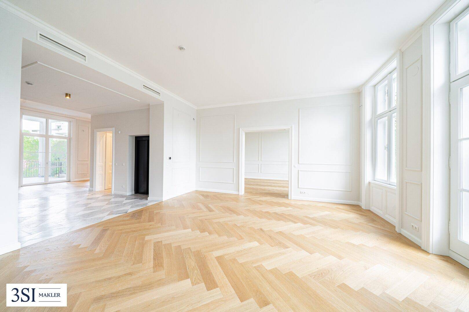 Großzügiges Wohnzimmer mit Fischgrätparkett, hohen Decken und eleganten Wandpaneelen.