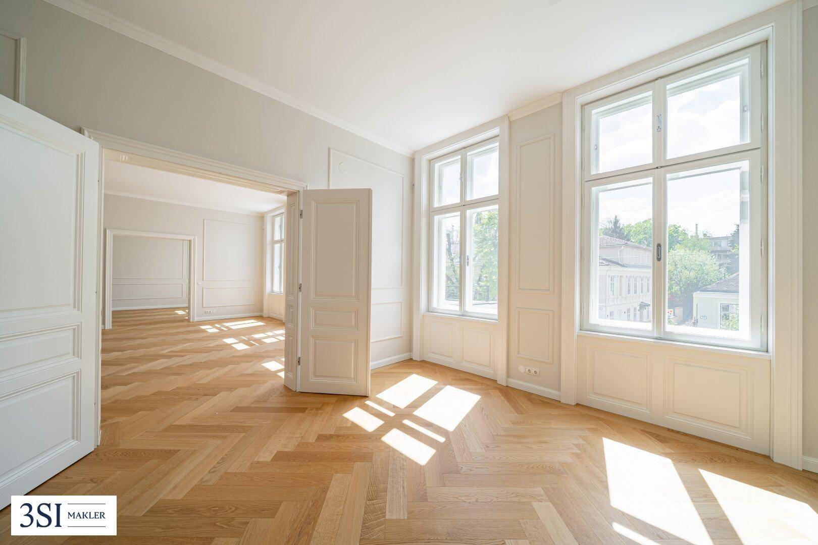 Lichtdurchfluteter Raum mit elegantem Fischgrätparkett, hohen Fenstern und sonniger Atmosphäre.