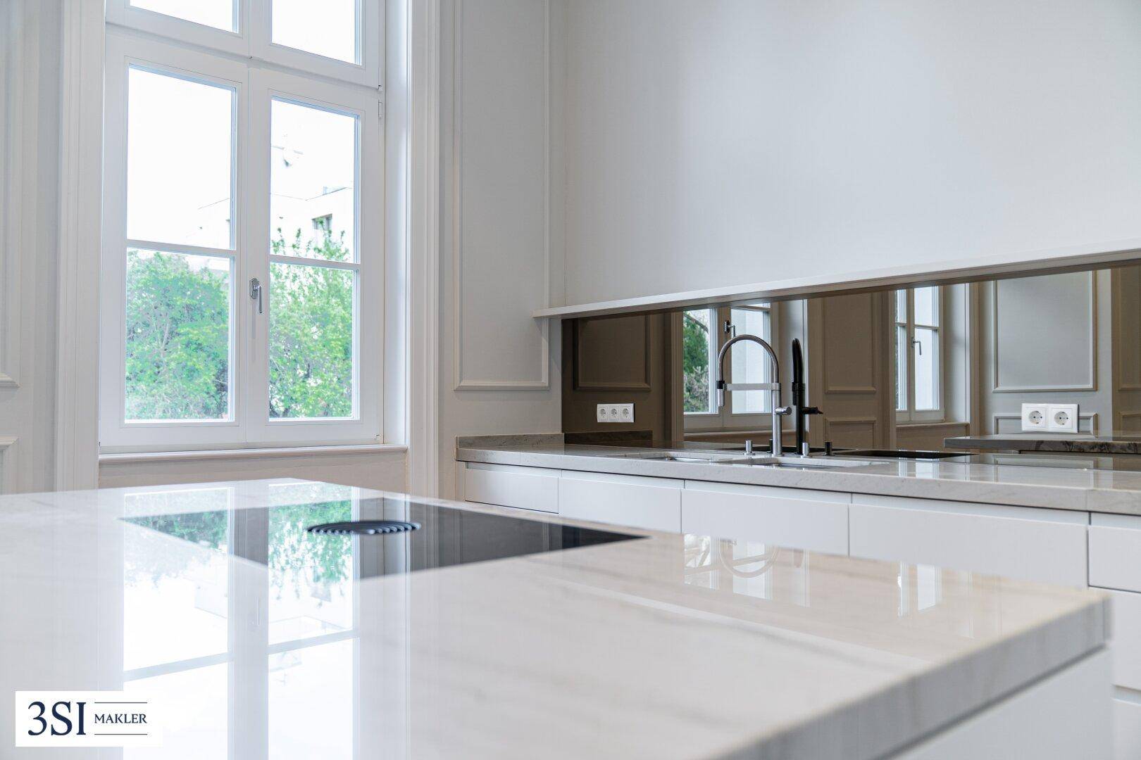 Moderne Küche mit weißer Arbeitsplatte, Induktionskochfeld und Spiegelfliesen als Spritzschutz.