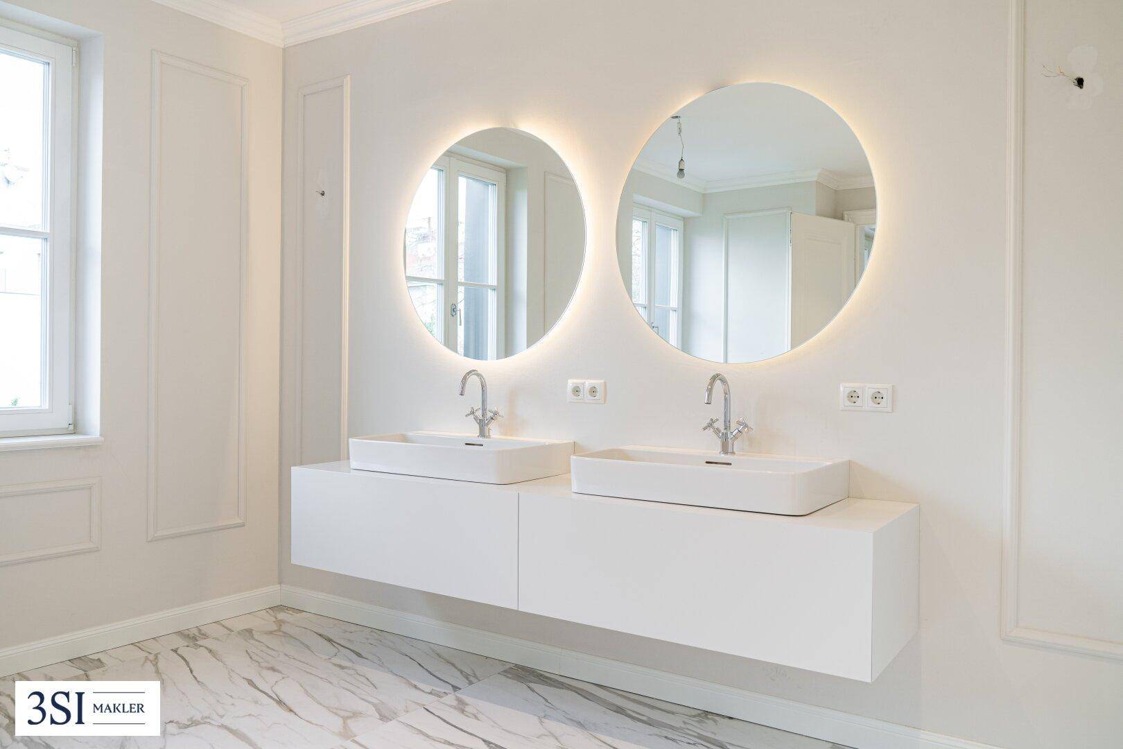 Modernes Badezimmer mit Doppelwaschbecken, beleuchteten Spiegeln und Marmorfliesen.