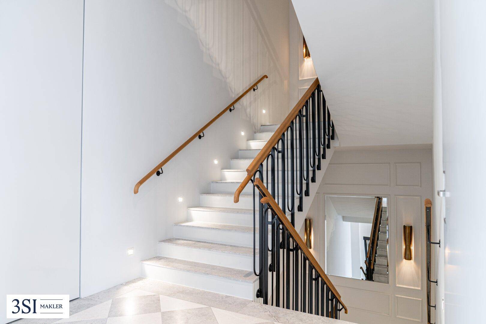 Elegantes Treppenhaus mit Marmorboden, Holzgeländer und indirekter Beleuchtung.