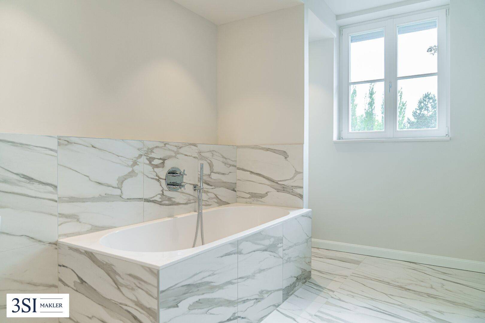 Helles Badezimmer mit Badewanne, Marmorfliesen und Fenster für Tageslicht.