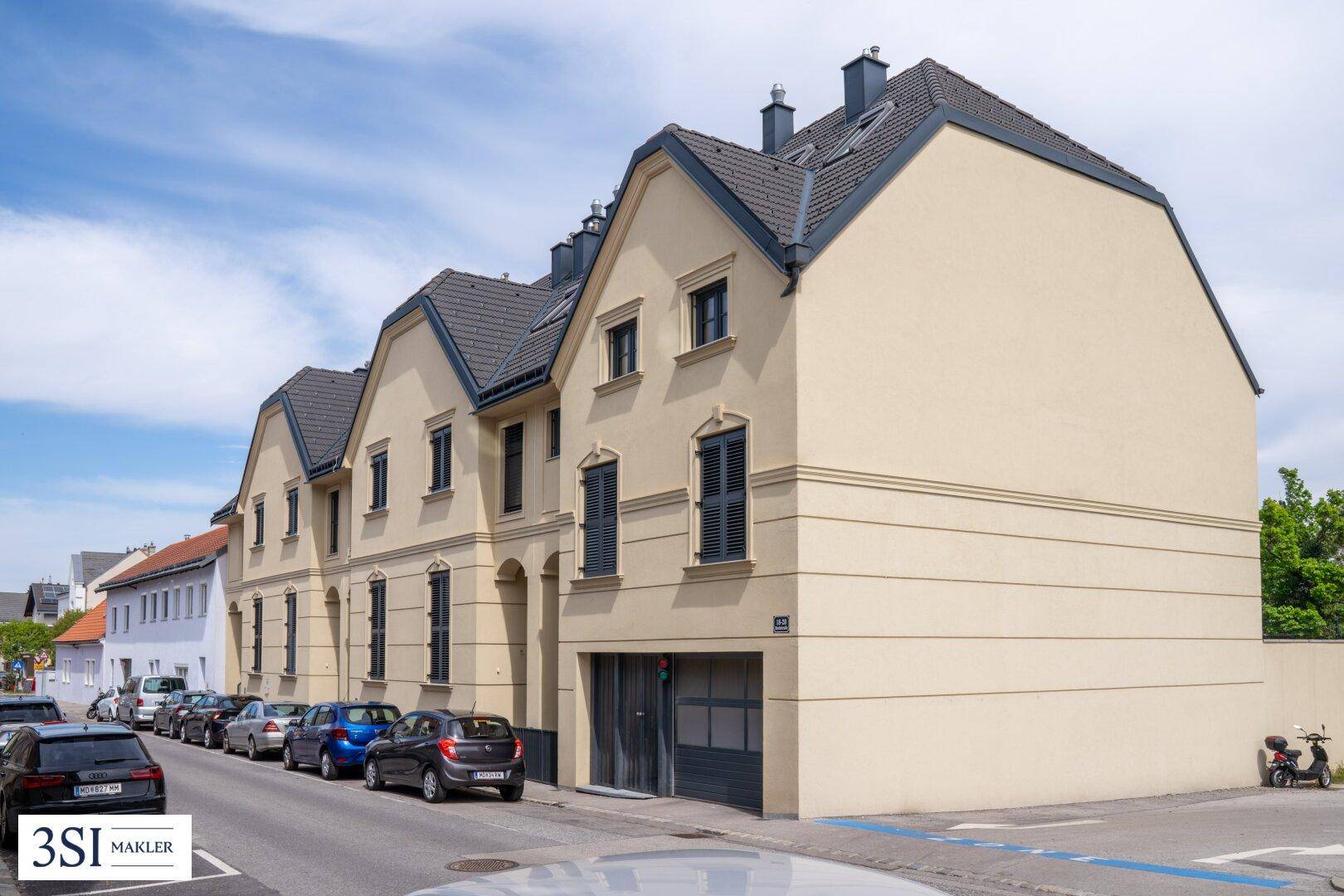 Ansicht der modernen Gebäudefassade von der Straße mit geparkten Autos und klarem Himmel.