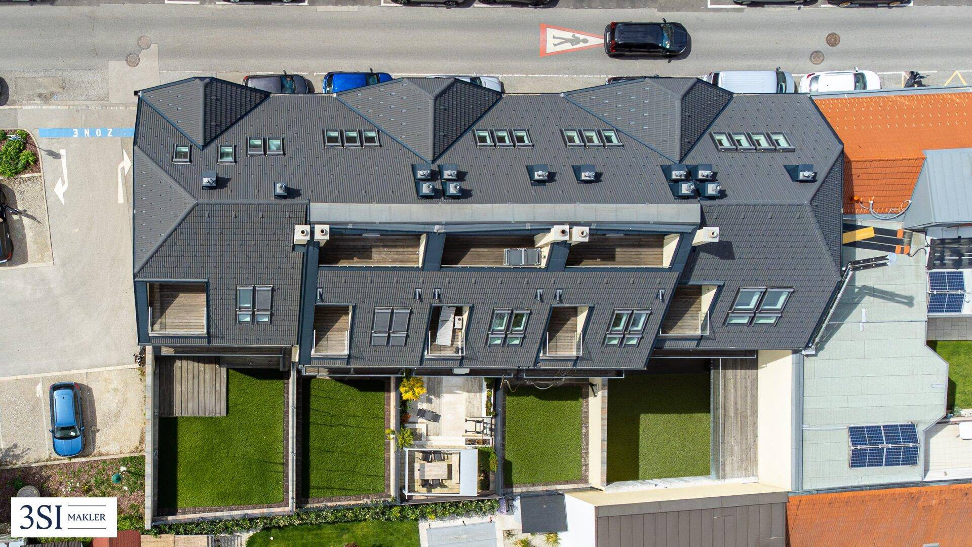 Luftaufnahme eines modernen Wohnkomplexes mit Gärten und Dachfenstern in städtischer Umgebung.