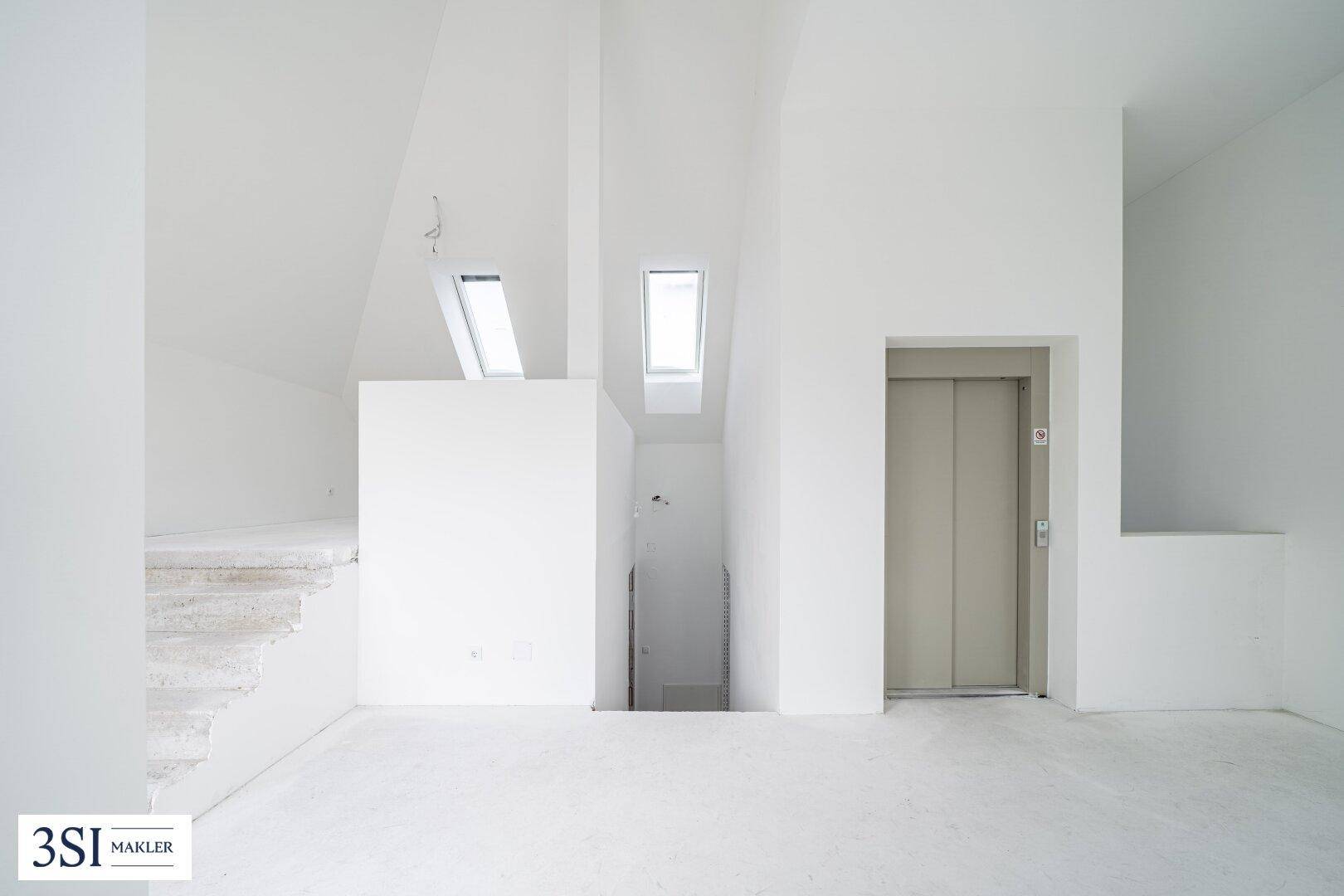 Heller Dachbodenraum mit schrägen Decken, Dachfenstern und Aufzug, bereit für den Ausbau.