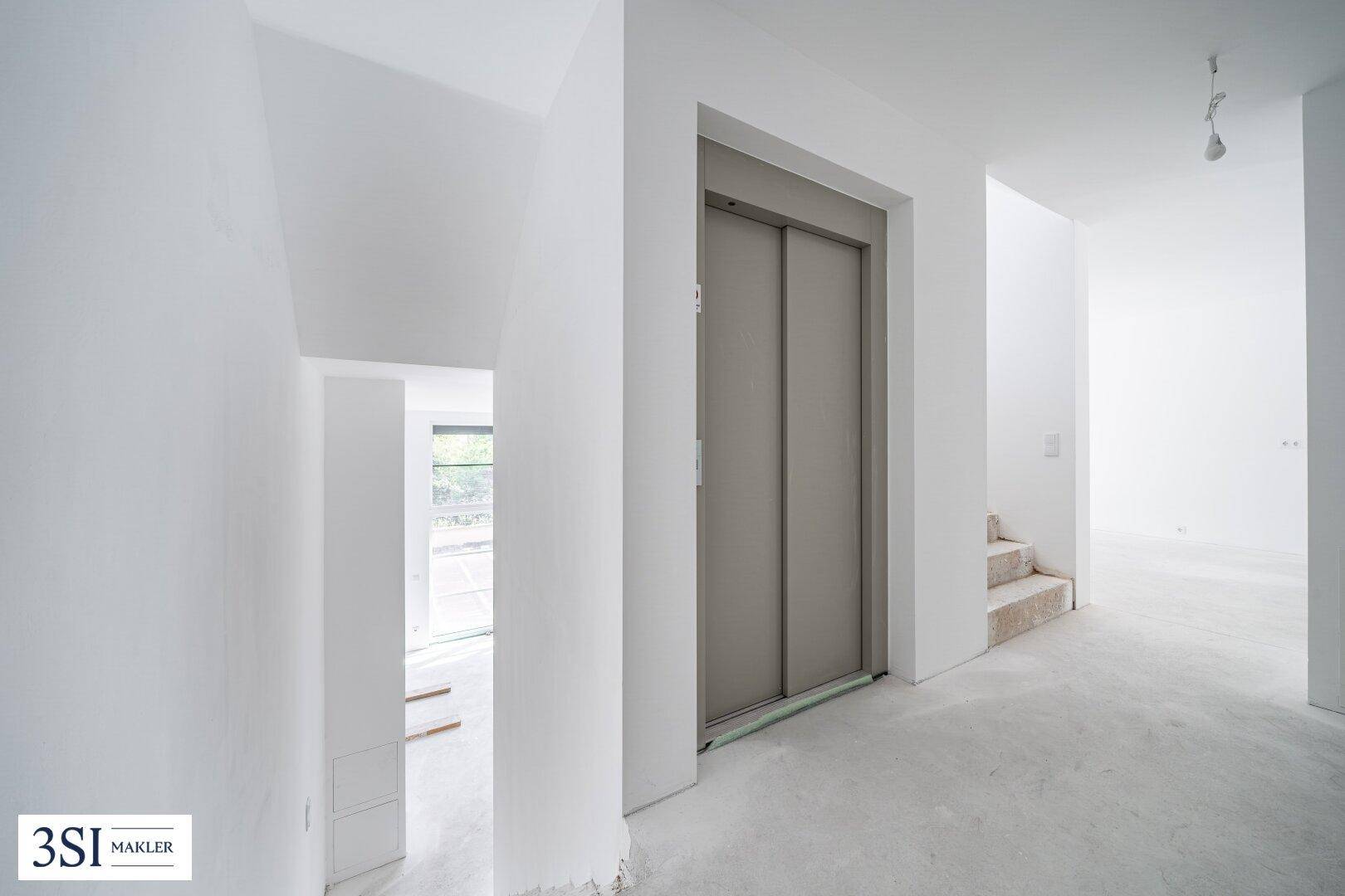 Heller Flur im Rohbauzustand mit sichtbarem Aufzug und Treppe, bereit für den Innenausbau.