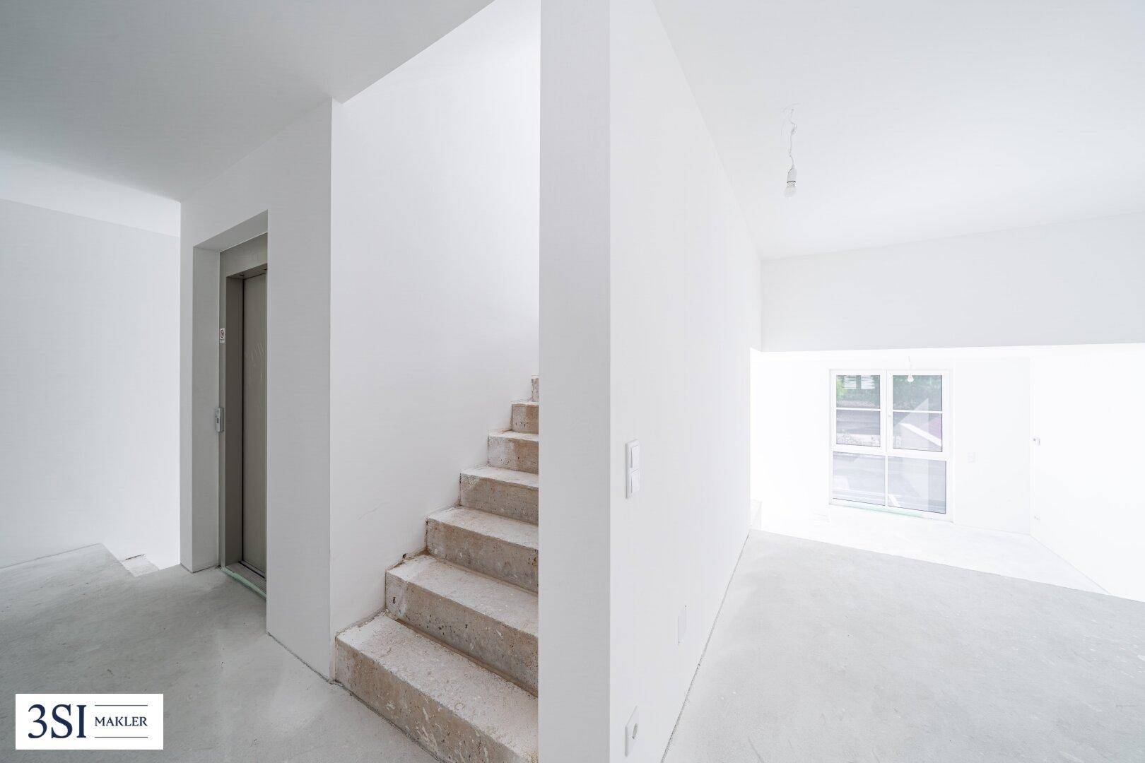 Geräumiger Flur im Rohbauzustand mit Aufzug und Treppe, ideal für den Zugang zu den Wohnungen.