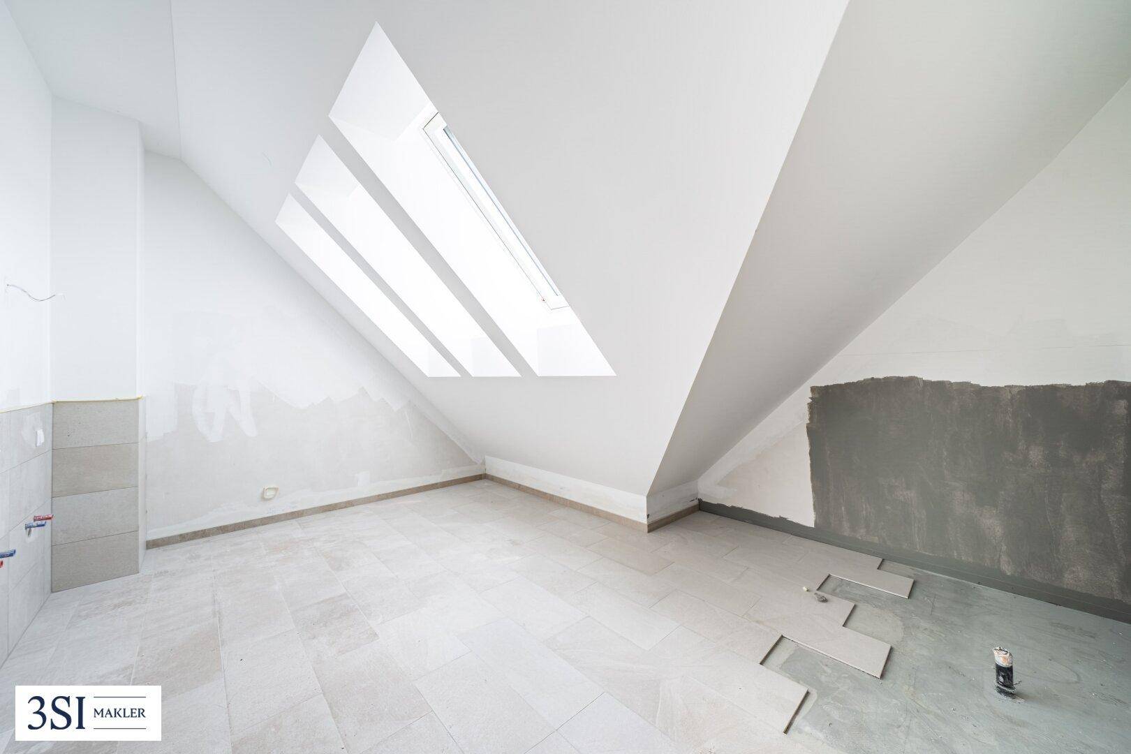 Unfertiger Dachbodenraum mit schrägen Wänden, Dachfenster und vorbereiteten Fliesen für den Ausbau.