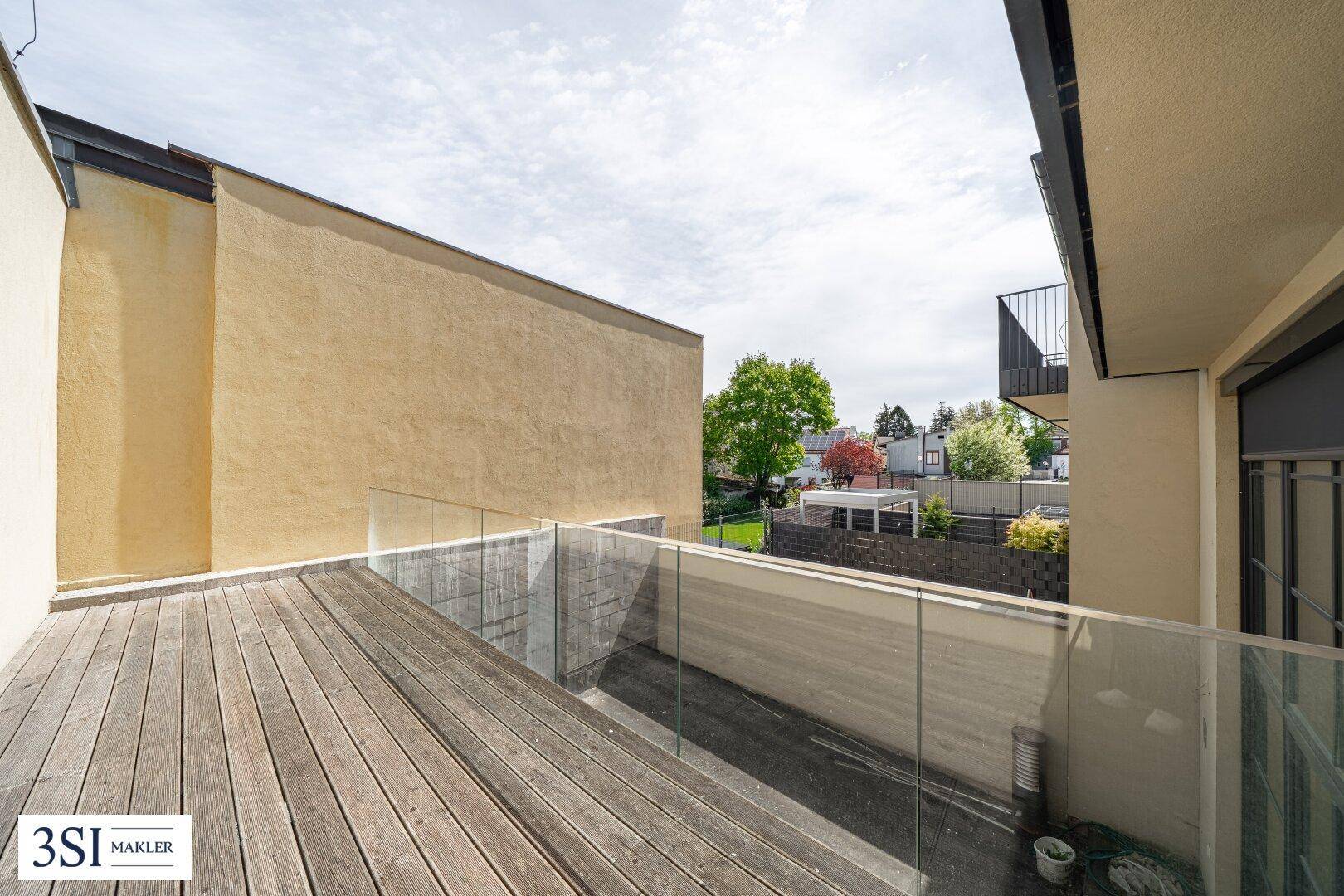 Geräumige Holzterrasse mit Glasgeländer und Blick auf die grüne Umgebung.