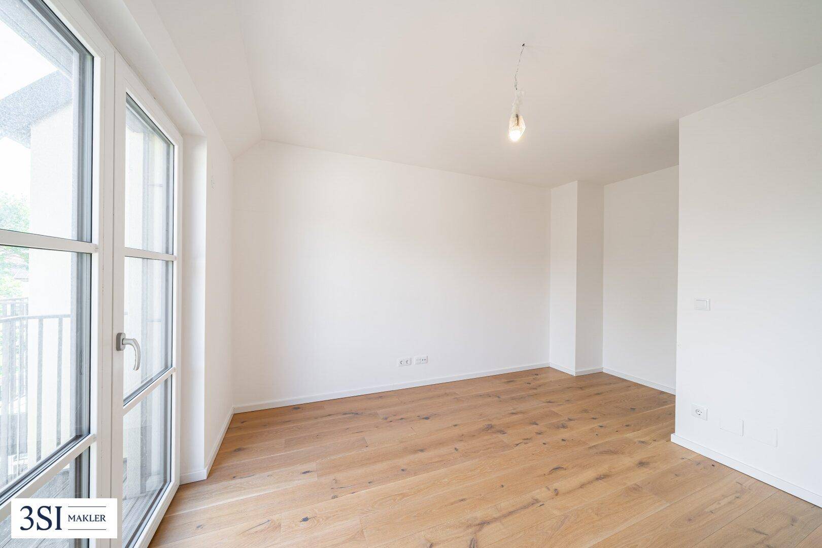 Helles Schlafzimmer mit Holzboden und Zugang zu einem Balkon, der viel Tageslicht hereinlässt.