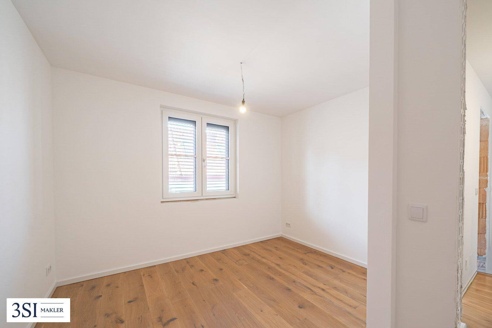 Helles Zimmer mit Holzboden und Fenster, bereit für die individuelle Gestaltung.