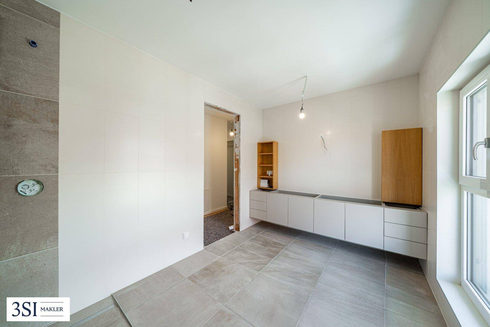 Raum im Rohbau mit Fliesenboden und vorbereiteten Wandinstallationen.